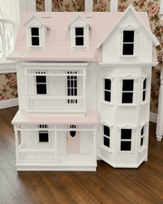 Detailed dollhouse with white exterior and pink roof on a wooden floor.